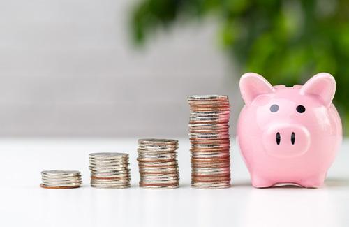 A pile of coins next to a piggy bank 