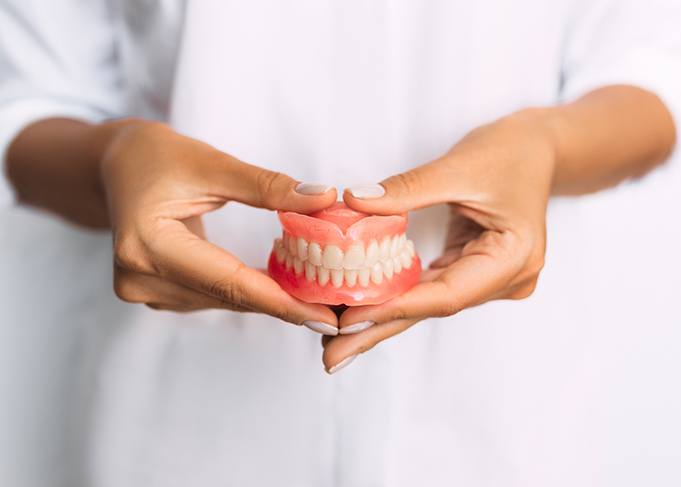 Closeup of two hands holding a complete set of dentures